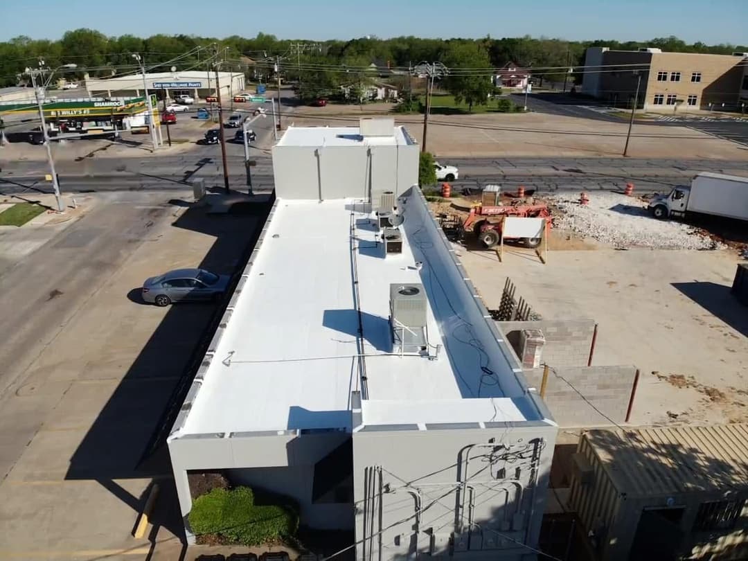 Aerial view of a commercial building's white roof with HVAC units, near a busy intersection.
