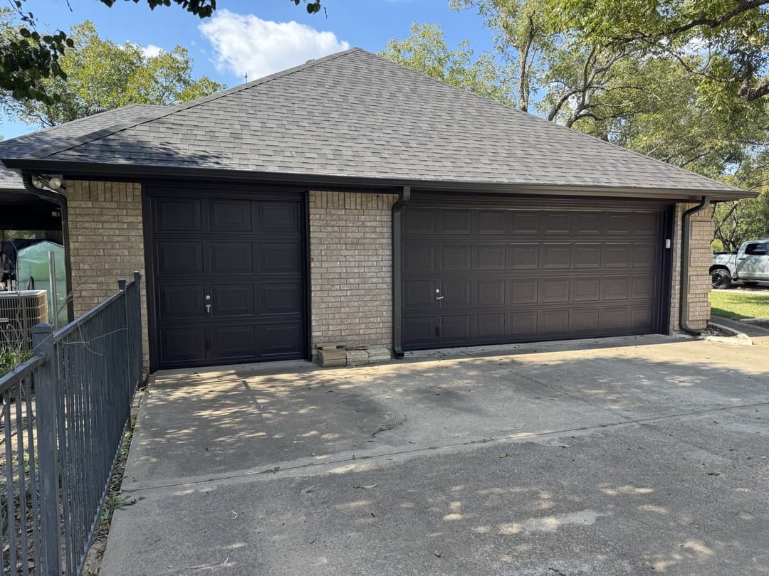 Two-car garage with brown doors, located beside a concrete driveway and surrounded by trees.